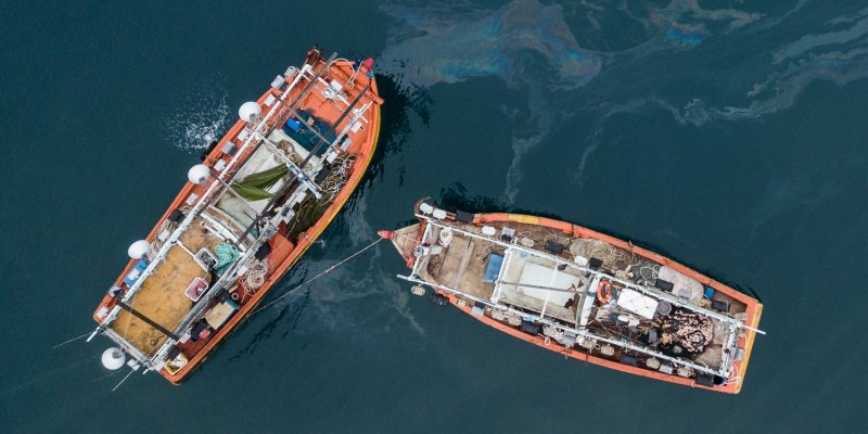 Two fishing boats side by side in the water with leaking oil into the water.